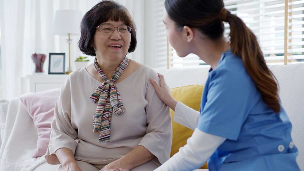 Three caregivers assist a group of older adults in a bright, residential common area.